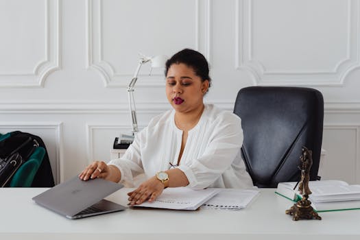 Confident businesswoman in a white blouse working at a stylish office desk with a laptop and legal documents.