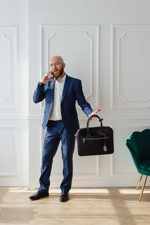 Free Professional bald bearded man in suit making a call holding a briefcase. Stock Photo