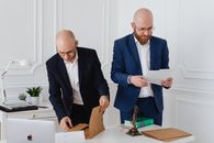 Two business professionals in corporate attire reviewing documents in a modern office setting.