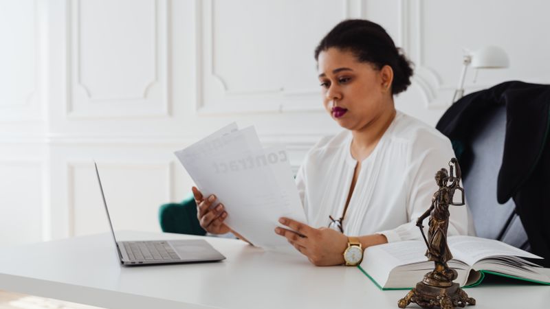 Black woman lawyer reading legal papers at her desk in a modern office.