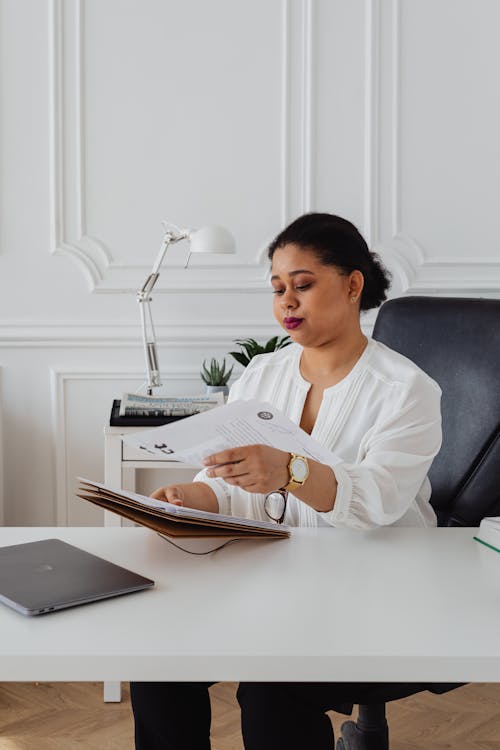 Free A Woman in the Office Sitting at the Desk Holding Documents Stock Photo