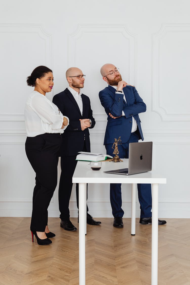 People In The Office Standing Near The White Desk With A Laptop