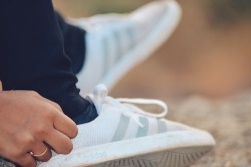 Free A detailed close-up of a person tying Adidas sneakers outdoors, showcasing a ring on the hand. Stock Photo