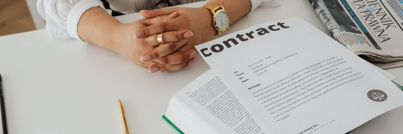 Businesswoman sitting at desk reviewing contract with legal documents and newspaper.