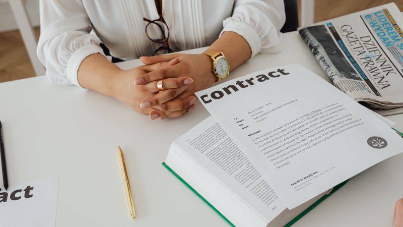 Businesswoman sitting at desk reviewing contract with legal documents and newspaper.