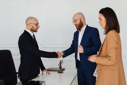 Three business professionals in formal attire shake hands during an office meeting.
