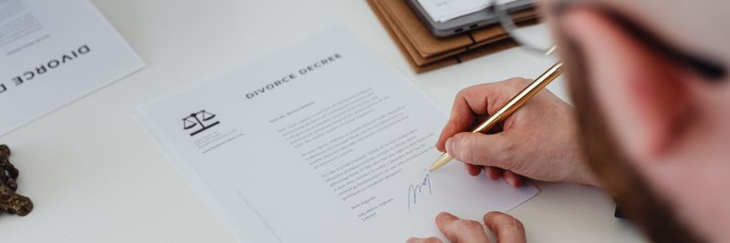 Close-up of a person signing a divorce decree on a desk.