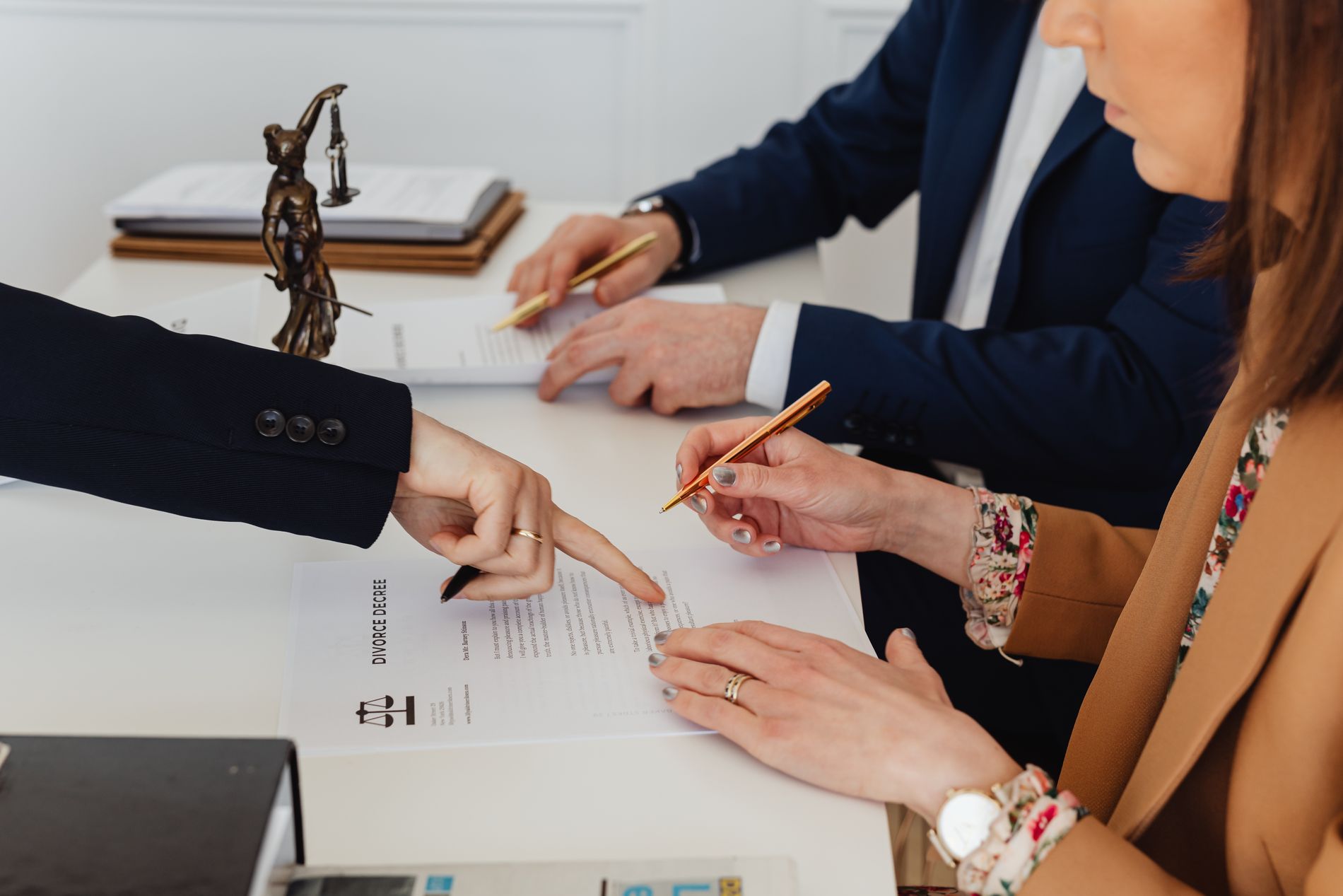 Hands signing legal documents beside a justice statue
