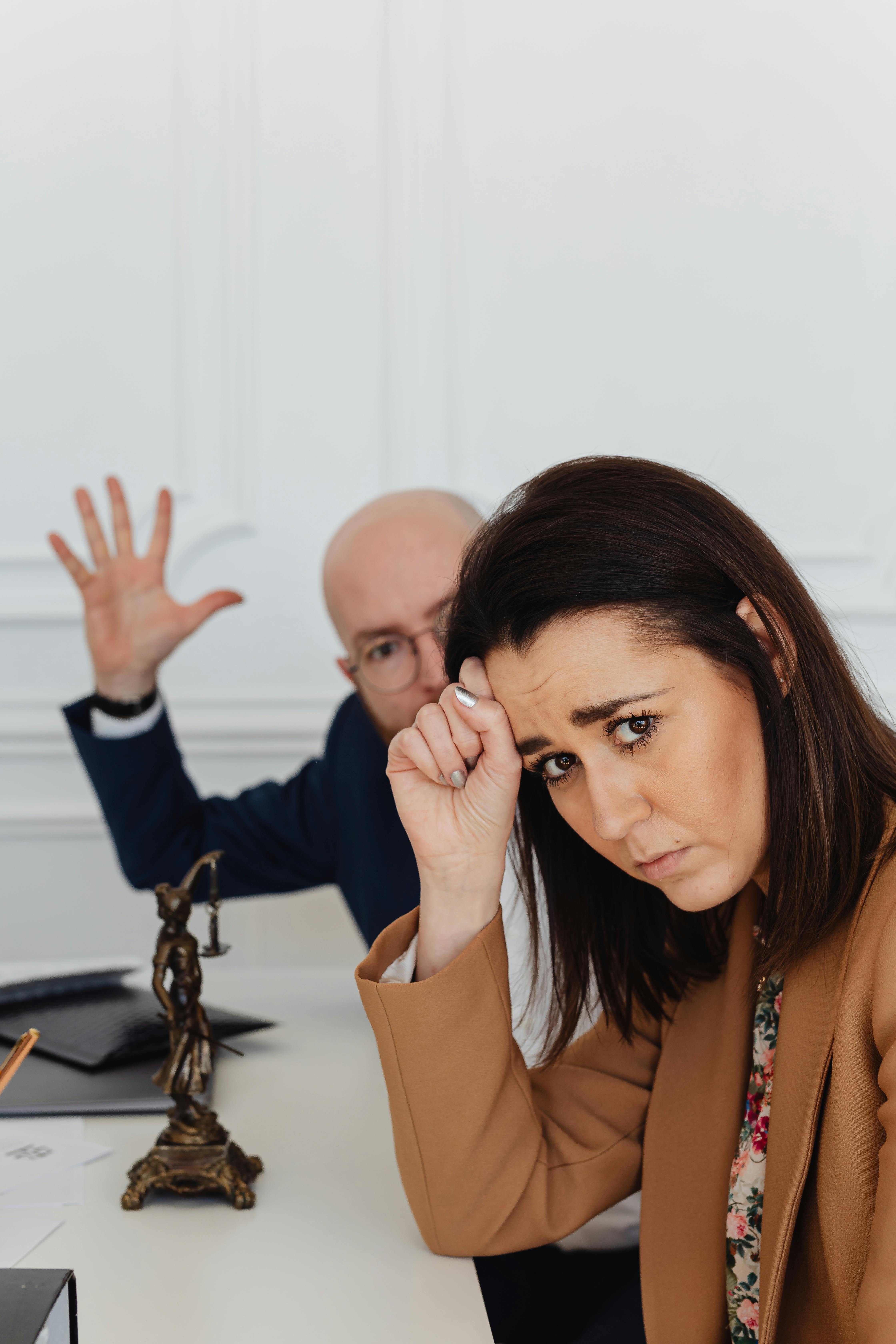A worried businesswoman sits at a desk in a modern office setting, depicting workplace stress.