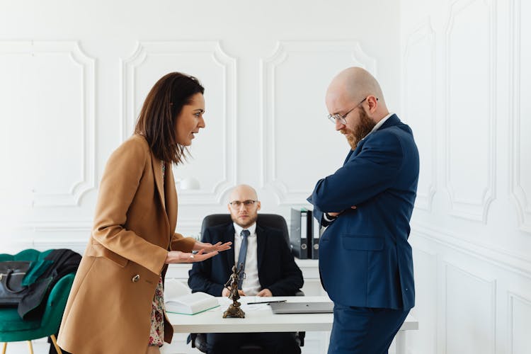 A Man Sitting At A Desk Looking At A Woman Talking To A Man Standing In Front