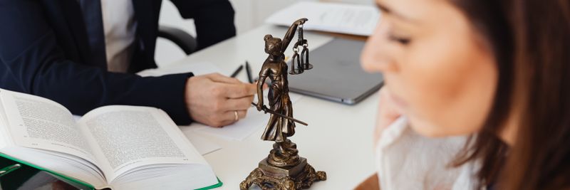 Two lawyers in an office, focusing on Lady Justice statue, discussing legal matters.