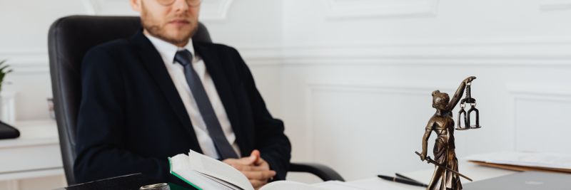 Bald lawyer in office sitting with legal documents and Justice statue.
