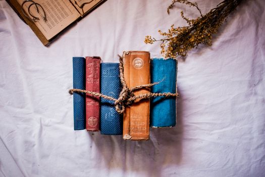 A stack of vintage books tied with string, accompanied by dried flowers on a fabric surface.