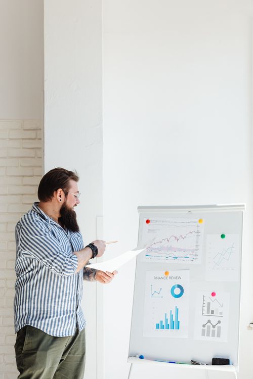 Free A bearded man presents financial charts and graphs, discussing data and statistics on a whiteboard. Stock Photo