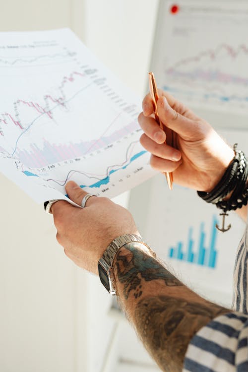 A Person Holding Pen and a Paper with Graphs