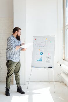 Bearded man reviewing financial charts in sunlit office space.