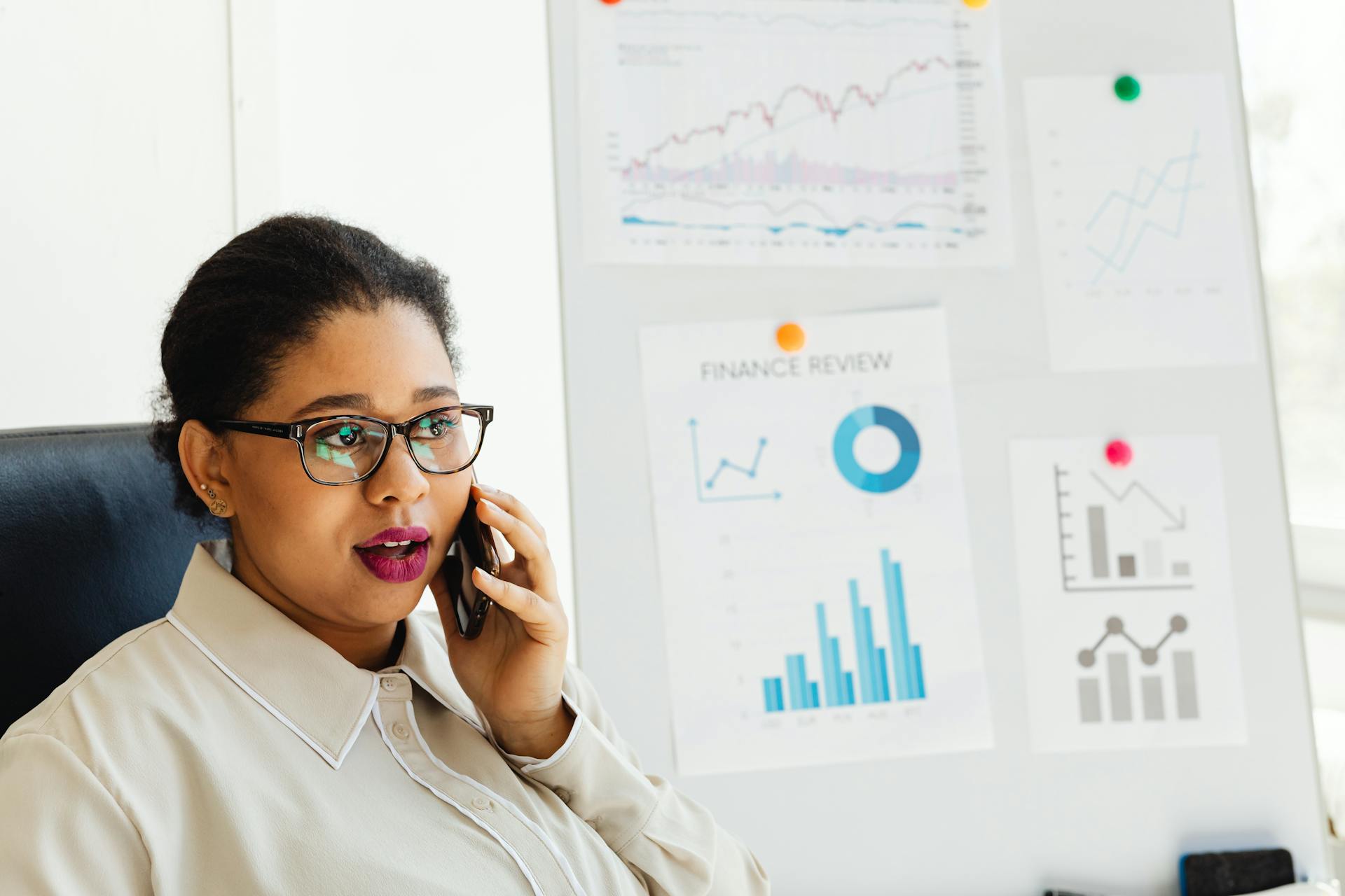 Focused businesswoman on call analyzing financial data displayed on whiteboard charts.