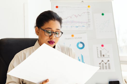 An African American woman studying financial charts and graphs in an office.