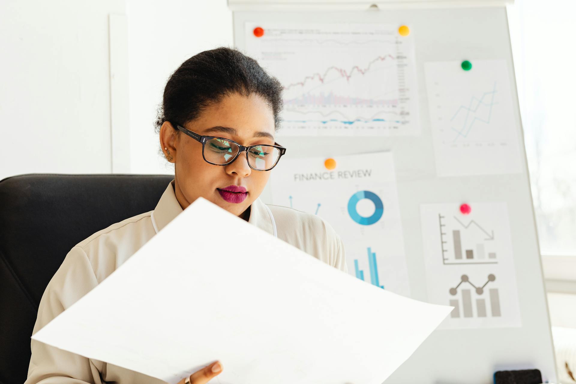 An African American woman studying financial charts and graphs in an office.