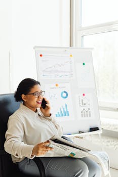 African American woman in office analyzing financial charts while using a smartphone.