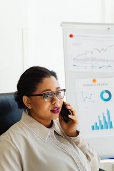 African American woman in office, analyzing finance charts on white board, talking on phone.