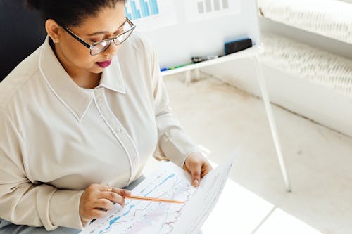 A Woman Wearing Eyeglasses Pointing a Pen on a Graph