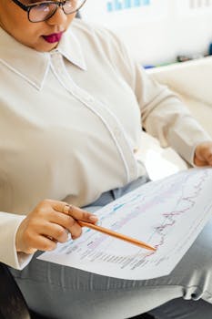 Focused businesswoman reviewing financial charts in an office setting with a pen.