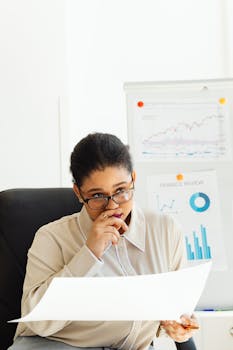 Woman analyzing financial charts with whiteboard in office, illustrating focus and strategy.