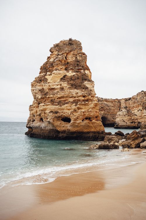 Free Scenic view of a towering rock formation on a tranquil beach with gentle waves. Stock Photo