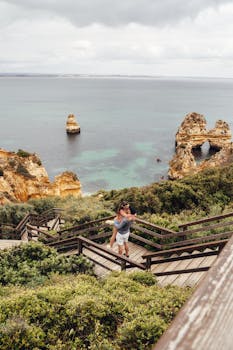Couple embracing on a wooden boardwalk overlooking cliffs and the ocean in Algarve, Portugal, showcasing love and travel.