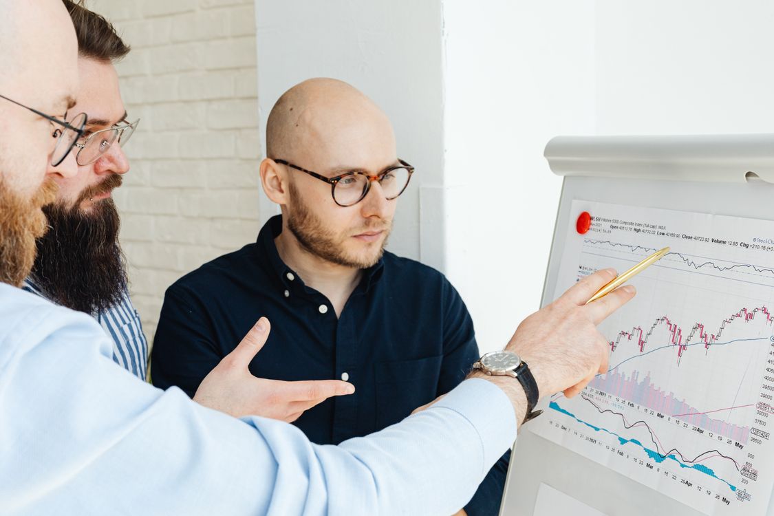 Free Three men discussing financial charts on a whiteboard during a business meeting. Stock Photo