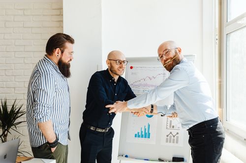 Free Three businessmen engage in a lively discussion around a whiteboard with charts in a sunlit office. Stock Photo