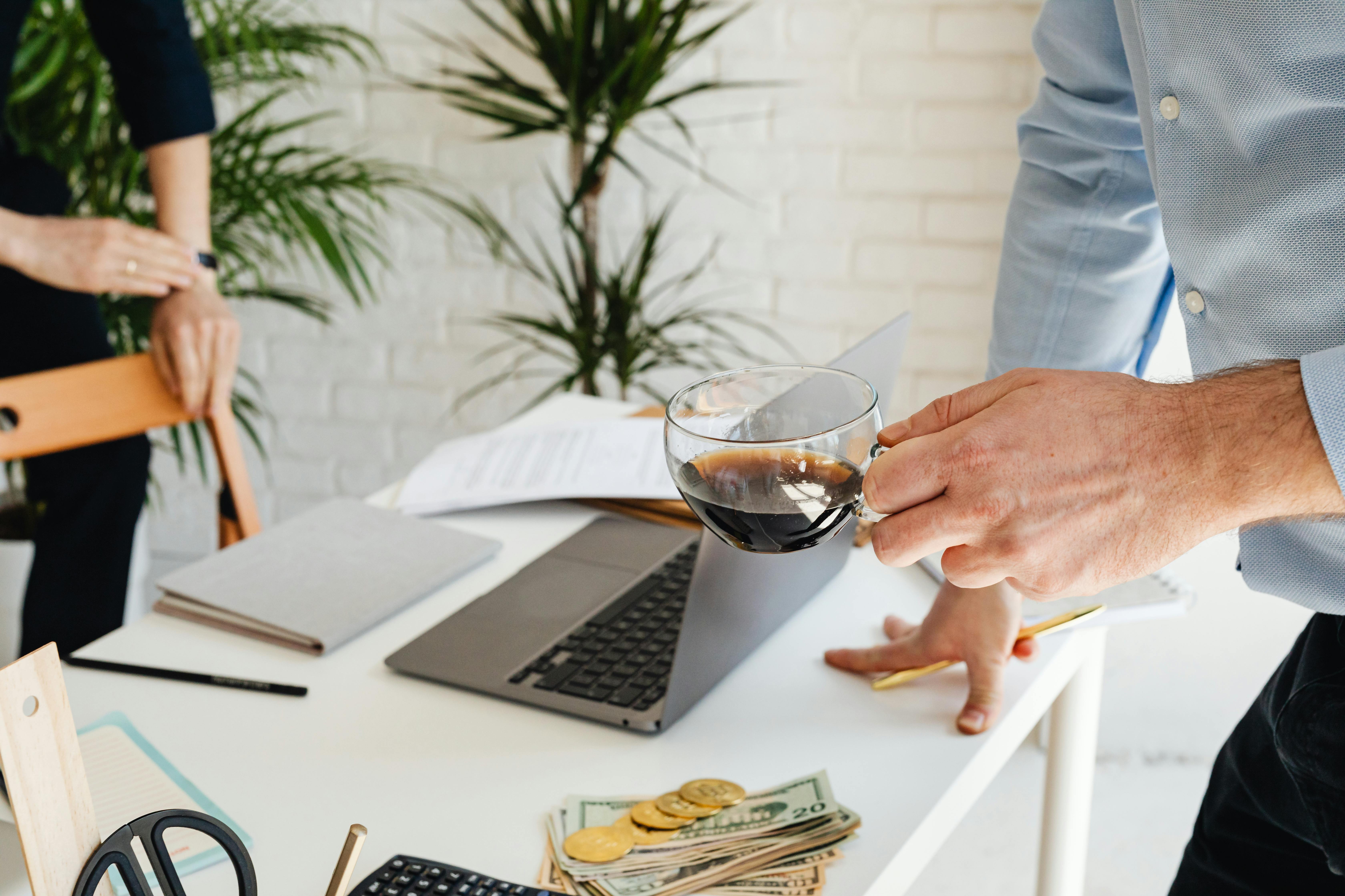 Two people working at an office desk with coffee, laptop, and financial documents.