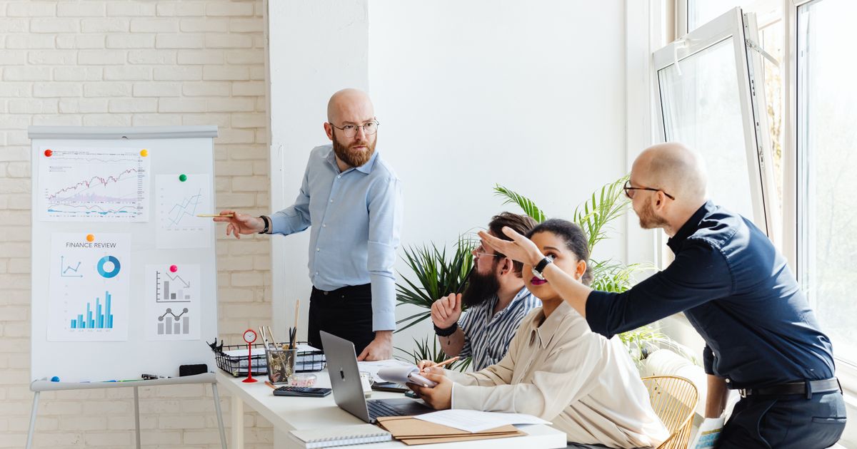 A group of professionals engaged in a business meeting, discussing financial graphs on a whiteboard.