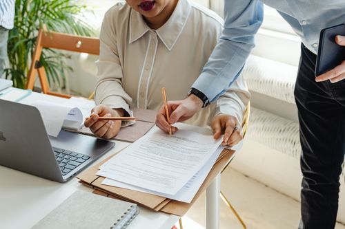 Free Two colleagues collaborating over documents and a laptop in a bright office setting. Stock Photo