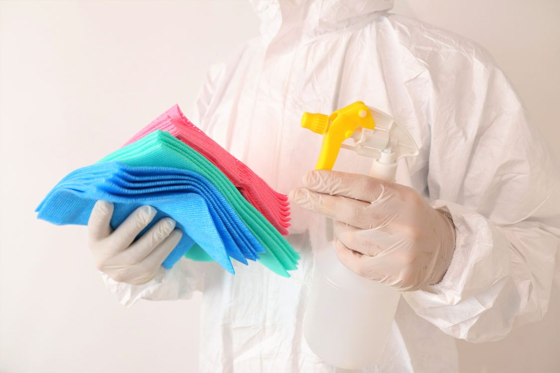 An image of a person wearing white overalls while holding colorful towels and a spray bottle