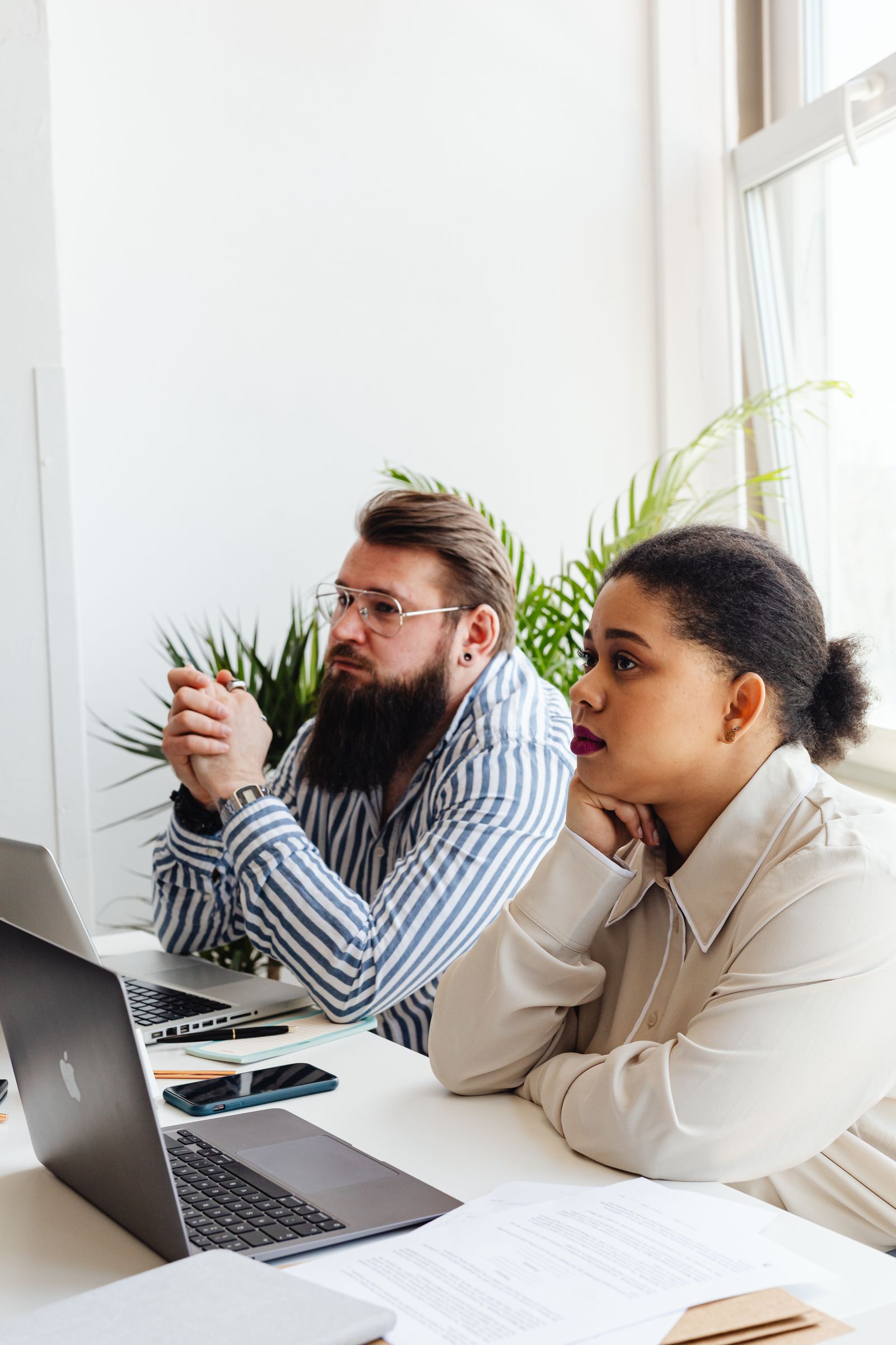 Free Two professionals in a bright office, deeply engaged in a discussion while working on laptops. Stock Photo