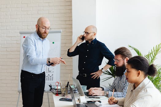 A group of four diverse adults collaborating in a modern office environment with laptops and charts.