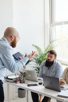 Three colleagues engaged in discussion at a modern office with laptops and plants.
