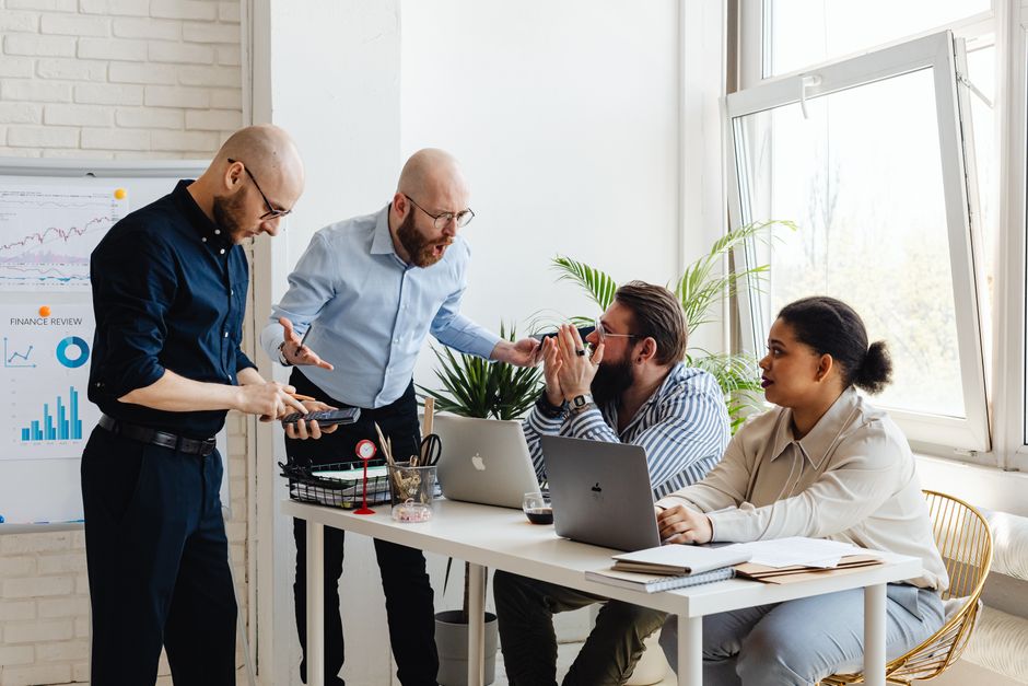 Group of diverse professionals engaged in a lively office discussion around a desk.