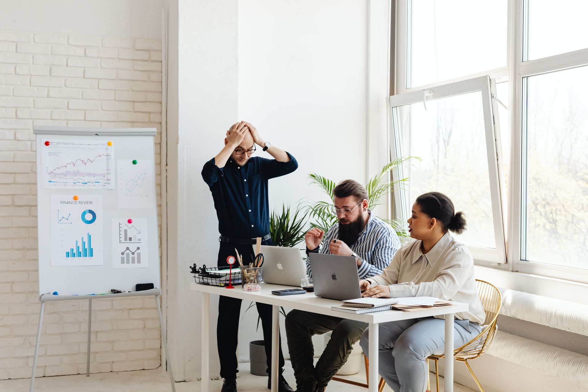 A multi-ethnic team working at an indoor office meeting with laptops and charts.