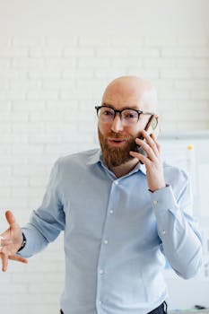 Bearded man in glasses having a serious phone conversation in office setting.