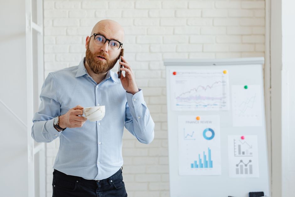 Business professional talking on the phone while holding a cup, with charts in the background. Business professional talking on the phone while holding a cup, with charts in the background.