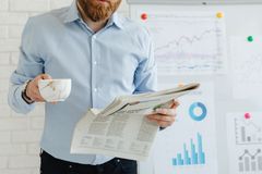 Business person holding coffee and newspaper in office with charts.