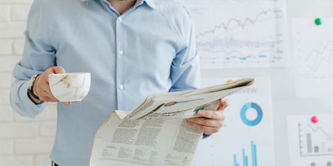 Business person holding coffee and newspaper in office with charts.