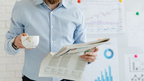 Business person holding coffee and newspaper in office with charts.