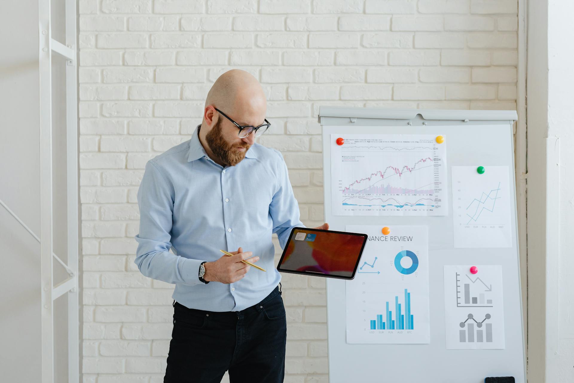 Bald man presenting finance data with tablet and graphs on whiteboard.