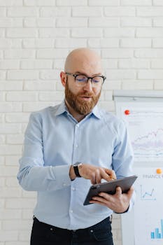 A businessman with glasses reviewing data on a tablet in an office setting.