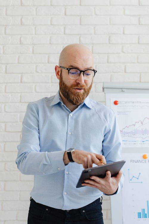 Free A businessman with glasses reviewing data on a tablet in an office setting. Stock Photo