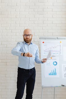 A bald man with eyeglasses checks his watch while analyzing data charts indoors.